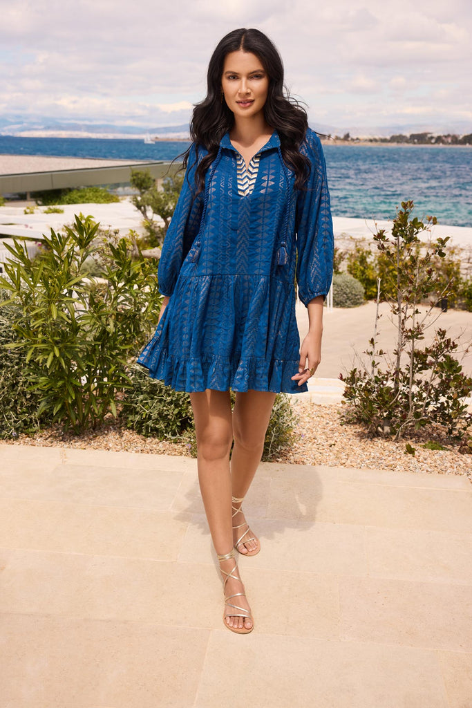 Woman on patio wearing a blue pull-over kimono swim dress with gold detailing on the front