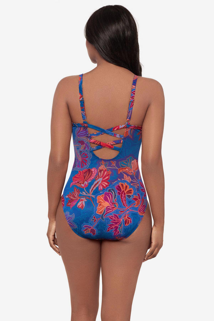 Woman turned away wearing a one-piece swimsuit with a red and orange flower print and lace-up back