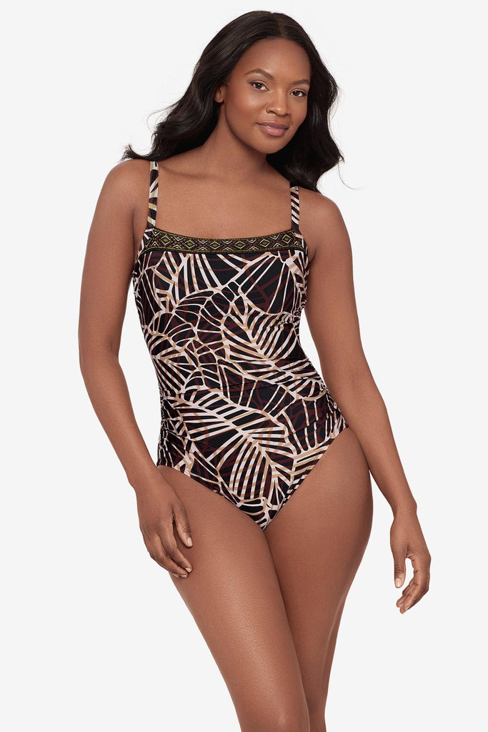 Woman wearing a brown abstract printed one-piece swimsuit with a detailed pattern on the neckline