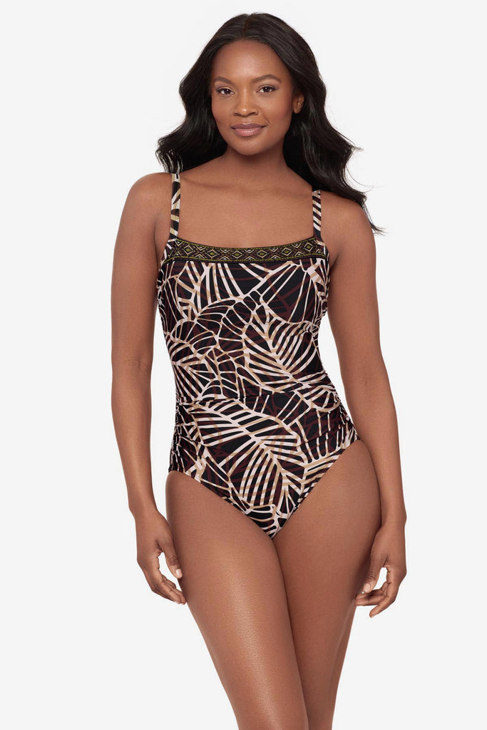 Woman wearing a brown abstract printed one-piece swimsuit with a detailed pattern on the neckline