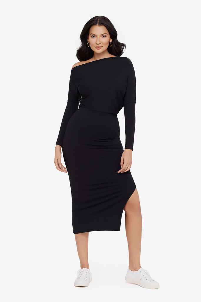 Woman wearing a black asymmetrical off the shoulder long sleeve dress with side slit