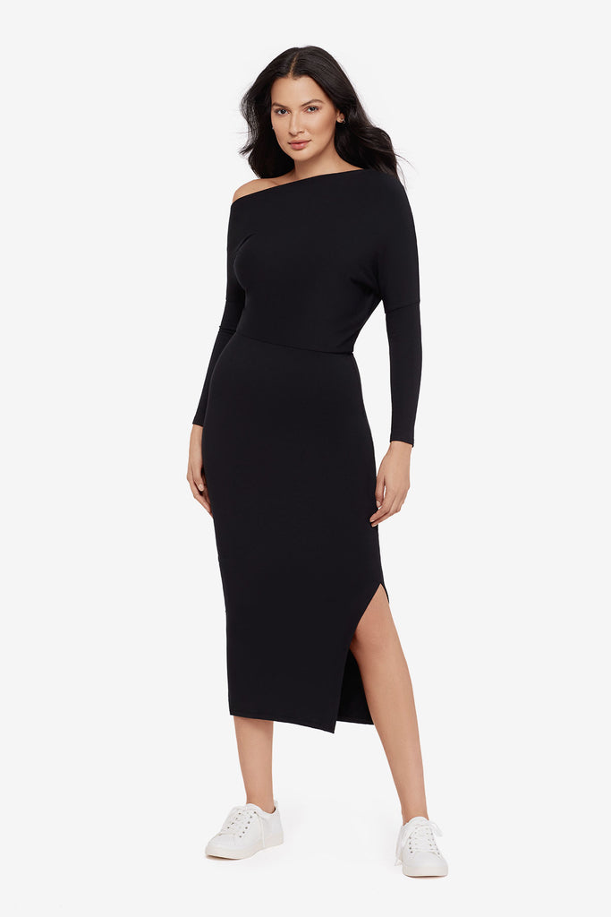 Woman wearing a black asymmetrical off the shoulder long sleeve dress with side slit