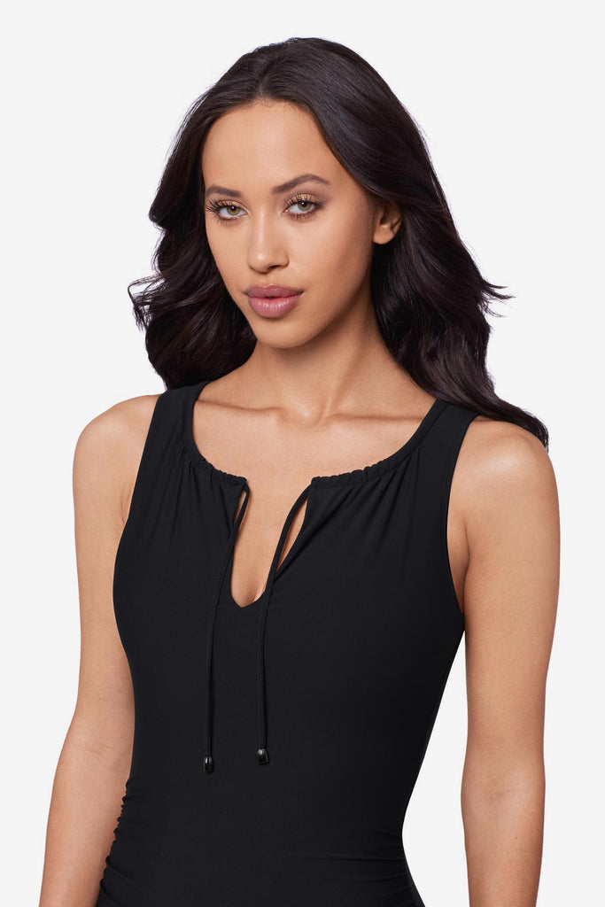 Close up of woman wearing a black one-piece swimsuit with tie detail at the neckline
