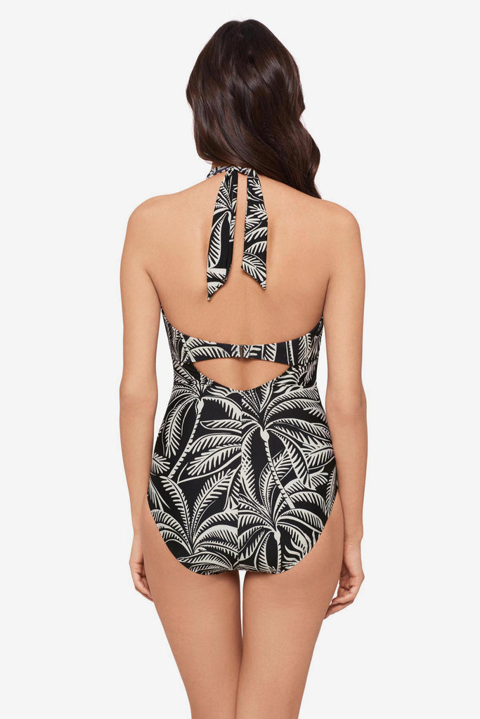 Woman turned away wearing a black and white palm leaf printed one-piece swimsuit with a halter tie