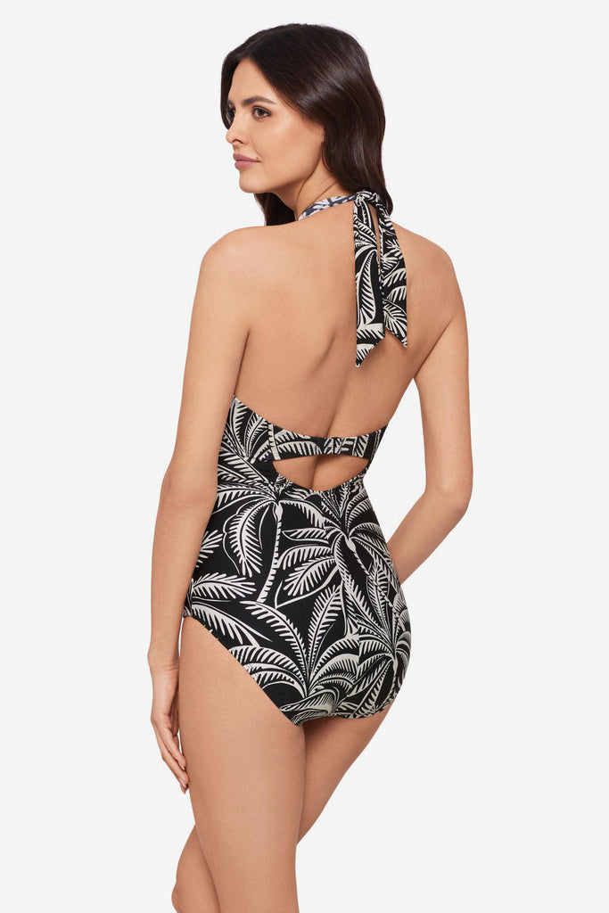 Woman turned left wearing a black and white palm leaf printed one-piece swimsuit with a halter tie
